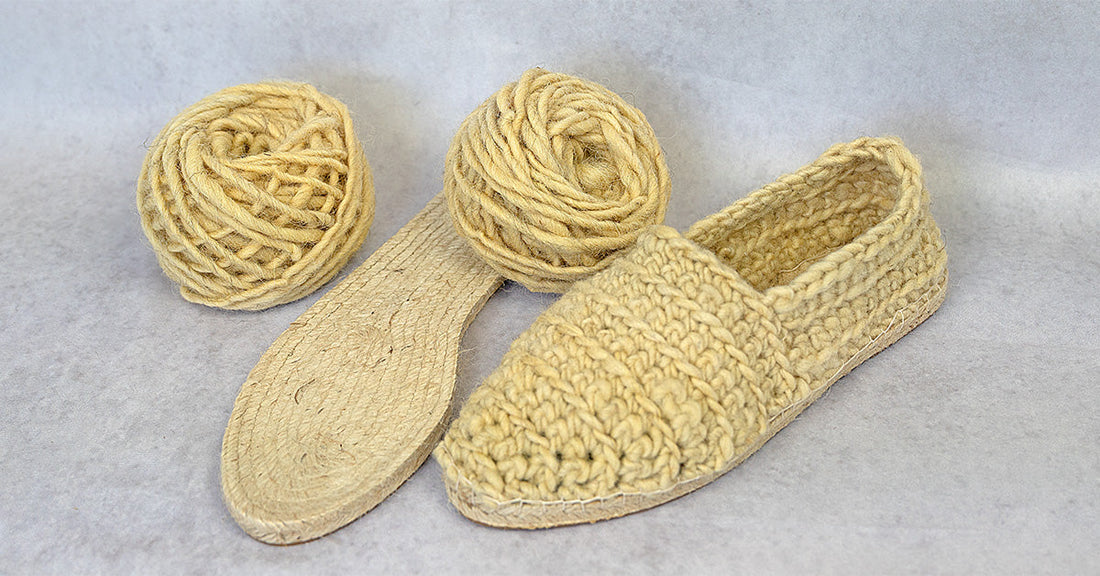 Gehäkelte Espadrilles aus naturbelassener Schafwolle, daneben Jutesohle und zwei passende Wollknäuel als DIY-Materialübersicht.